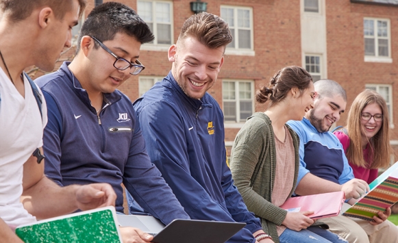 Group of students sitting on brick ledge reading books