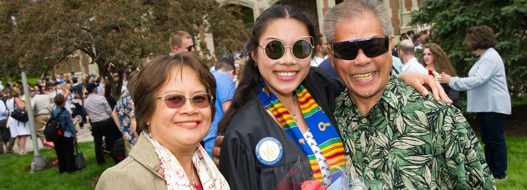 Parents with their daughter at graduation, she's holding flowers and her diploma and wearing a pin that says, "I did it!"