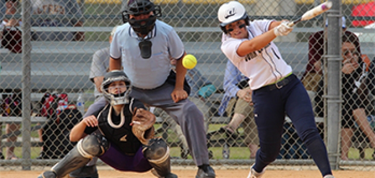 Softball player making connection for a hit before running to first base with catcher and umpire in the background